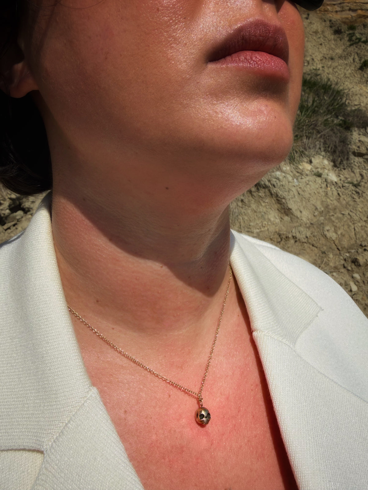 Closeup of a woman wearing A handmade 9ct gold skull drop necklace by Virginia Allan — luxury dark jewellery hallmarked in London