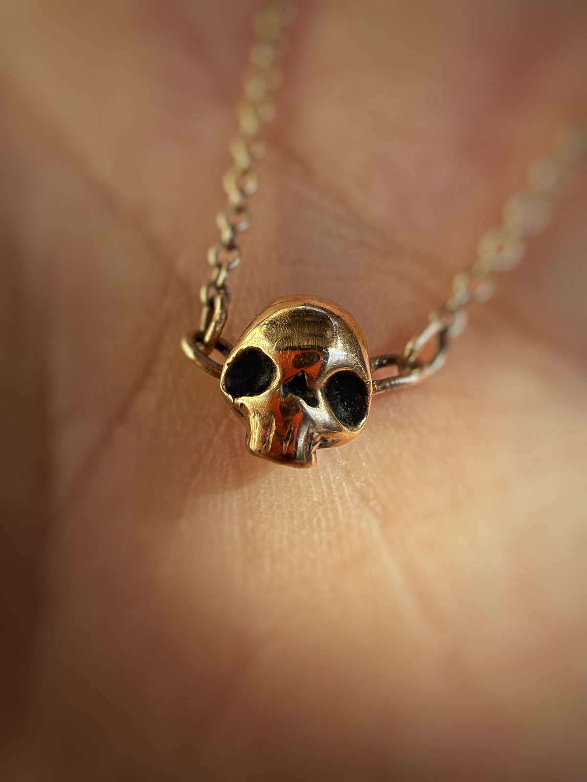 A small gold skull pendant necklace with blackened eye sockets, resting on a person's skin.