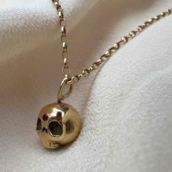 video of a gold skull necklace with a small inset ruby