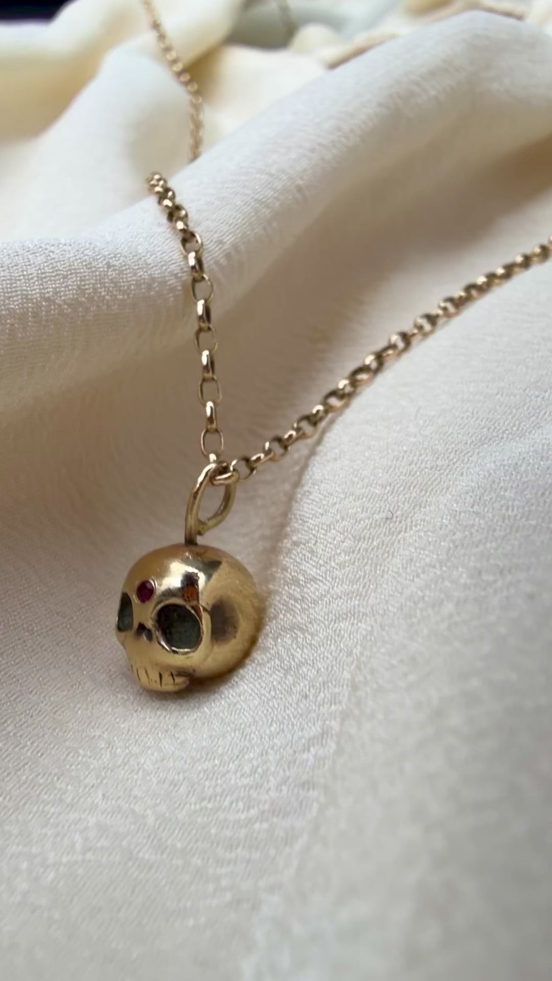 video of a gold skull necklace with a small inset ruby
